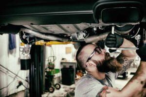 owner working under a car with hand tools looking up